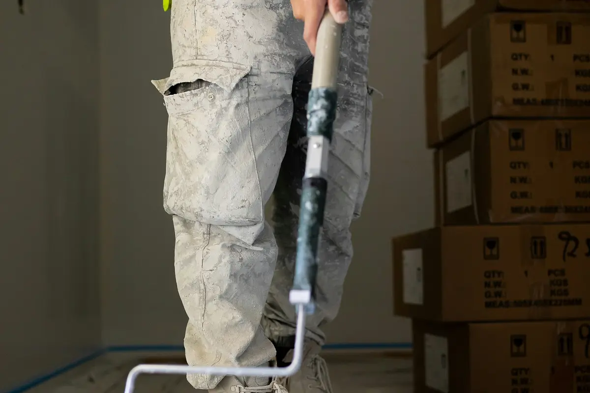 Pintor com rolo e bandeja em ambiente forrado para pintura