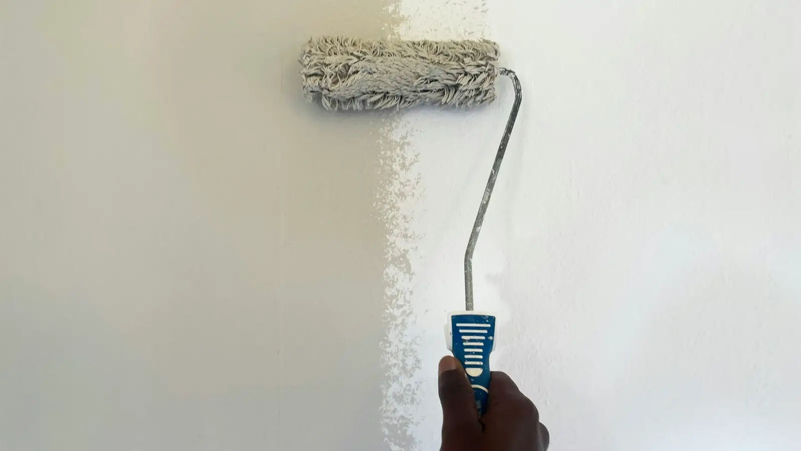 Mão passando rolo de tinta em parede meio pintada