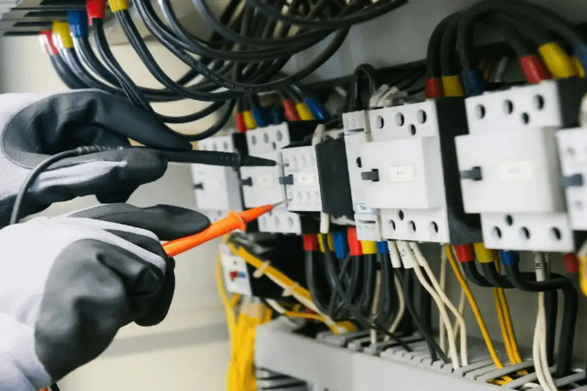 Técnico de luvas medindo o painel elétrico com multímetro
