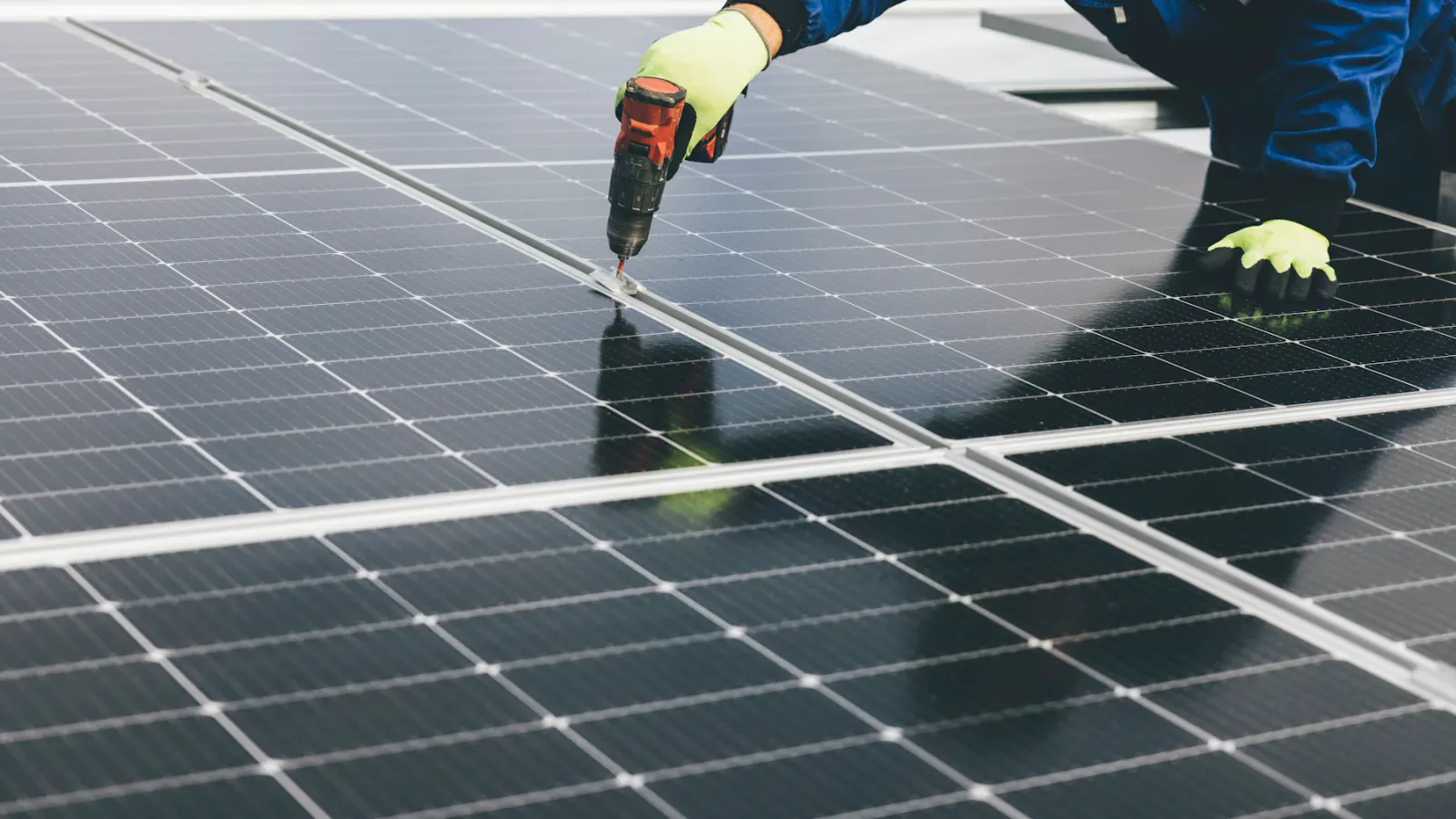 Mãos fixando painel solar com parafusadeira no telhado